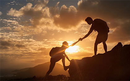 person giving a helping hand climbing a mountain at sunset