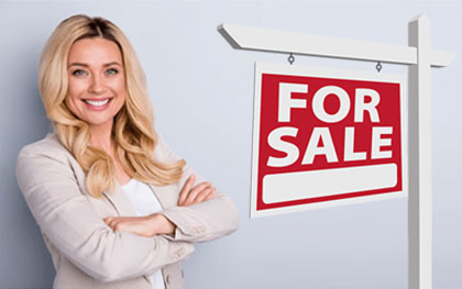 female real estate agent next to for sale sign