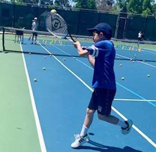 young boy hitting a tennis ball